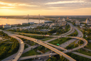 Aerial view of a Coastal Georgia waterfront city with highways, bridges, traffic, and regional infrastructure at golden hour.